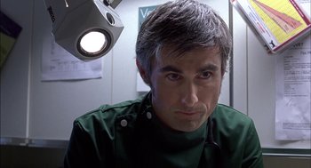 Movie still from “Notes on a Scandal” (2006), directed by Richard Eyre – A man in a green shirt is in a room; Close Up shot, Low angle