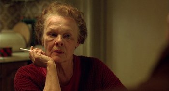 Movie still from “Notes on a Scandal” (2006), directed by Richard Eyre – An older woman sitting at a table with her chin resting on her hand; Close Up shot, Over the shoulder angle
