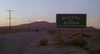 Movie still from “Nothing to Lose” (1997), directed by Steve Oedekerk – A road sign on the side of the road in the desert; Extreme Wide shot, Low angle