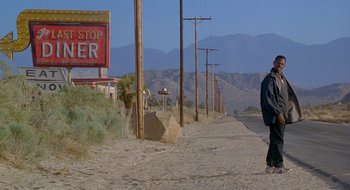 Movie still from “Nothing to Lose” (1997), directed by Steve Oedekerk – A person walking down a dirt road near a sign; Extreme Wide shot, Low angle