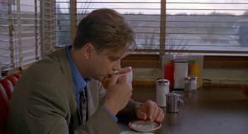 Movie still from “Nothing to Lose” (1997), directed by Steve Oedekerk – A man sitting at a table drinking a cup of coffee; Medium shot, Over the shoulder angle