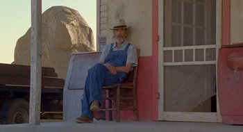 Movie still from “Nothing to Lose” (1997), directed by Steve Oedekerk – An older man sitting on a wooden chair outside; Wide shot, Low angle