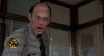 Movie still from “Nothing to Lose” (1997), directed by Steve Oedekerk – A man in a sheriff's uniform is making an angry face; Close Up shot, Over the shoulder angle