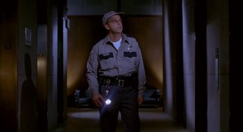 Movie still from “Nothing to Lose” (1997), directed by Steve Oedekerk – A police officer standing in a hallway holding a flashlight; Medium shot, Low angle