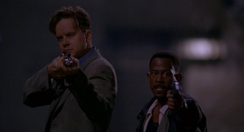 Movie still from “Nothing to Lose” (1997), directed by Steve Oedekerk – A man holding a gun next to another man holding a gun; Medium shot, Low angle