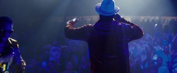 Movie still from “Notorious” (2009), directed by George Tillman Jr. – A man wearing a blue hat is holding a microphone in front of a group of onlookers; Medium shot, Low angle