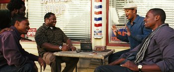 Movie still from “Notorious” (2009), directed by George Tillman Jr. – Two men sitting at a table in front of a barber shop; Medium shot, Over the shoulder angle