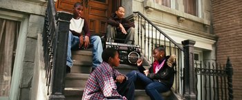 Movie still from “Notorious” (2009), directed by George Tillman Jr. – A group of young people sitting on the steps of a building; Medium shot, Low angle