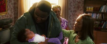 Movie still from “Notorious” (2009), directed by George Tillman Jr. – A man holding a baby while a woman looks on; Medium shot, Over the shoulder angle