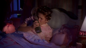 Movie still from “Now and Then” (1995), directed by Lesli Linka Glatter – A woman in a pink dress is in bed with a cell phone in her hand; Medium shot, High angle