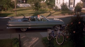 Movie still from “Now and Then” (1995), directed by Lesli Linka Glatter – A man driving a car down a street next to bicycles; Wide shot, High angle