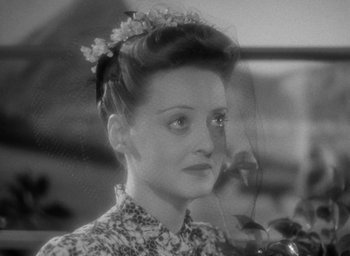 Movie still from “Now, Voyager” (1942), directed by Irving Rapper – A black and white photo of a woman with a flower in her hair; Close Up shot, High angle
