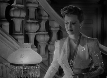 Movie still from “Now, Voyager” (1942), directed by Irving Rapper – A black and white photo of a woman looking at a lamp; Medium shot, High angle