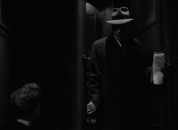 Movie still from “Now, Voyager” (1942), directed by Irving Rapper – A black and white photo of a man in a suit and a hat; Medium shot, Over the shoulder angle