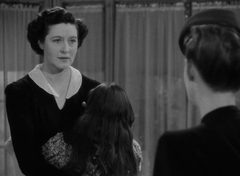 Movie still from “Now, Voyager” (1942), directed by Irving Rapper – An old black and white photo of a woman talking to two young girls; Medium shot, Over the shoulder angle