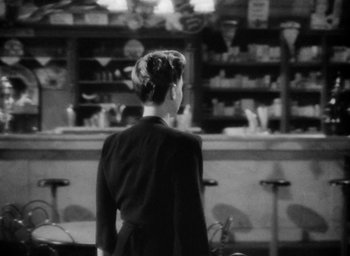 Movie still from “Now, Voyager” (1942), directed by Irving Rapper – A woman standing in front of a counter; Medium shot, Over the shoulder angle