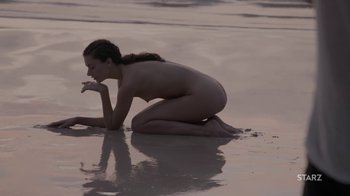 Movie still from “Nude” (2017), directed by Tony Sacco – A naked woman kneeling on the beach in the water; Wide shot, High angle