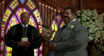 Movie still from “Nutty Professor II: The Klumps” (2000), directed by Peter Segal – A man in a suit and tie standing in front of a stained glass window; Medium shot, Low angle