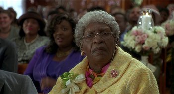 Movie still from “Nutty Professor II: The Klumps” (2000), directed by Peter Segal – An older woman wearing a yellow jacket and a pink and white flower in her hair; Close Up shot, High angle