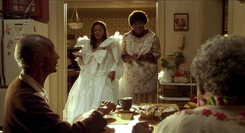 Movie still from “Nutty Professor II: The Klumps” (2000), directed by Peter Segal – Two women standing next to each other in front of a table; Medium shot, Over the shoulder angle