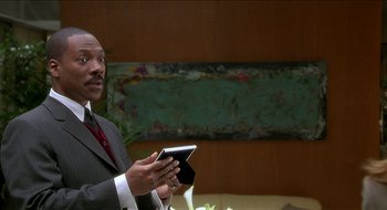 Movie still from “Nutty Professor II: The Klumps” (2000), directed by Peter Segal – A man in a suit holding a cell phone; Medium shot, Over the shoulder angle
