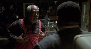 Movie still from “Nutty Professor II: The Klumps” (2000), directed by Peter Segal – An older man talking to another man in a workshop; Medium shot, Over the shoulder angle