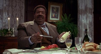 Movie still from “Nutty Professor II: The Klumps” (2000), directed by Peter Segal – A man sitting at a dinner table holding a knife and fork; Medium shot, High angle