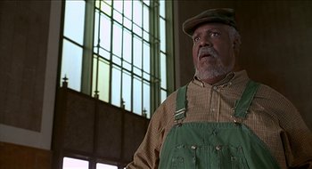Movie still from “Nutty Professor II: The Klumps” (2000), directed by Peter Segal – An older man wearing a hat standing in front of a window; Medium shot, Low angle