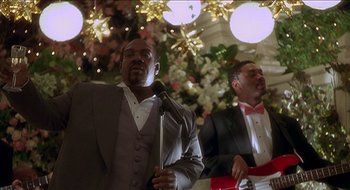 Movie still from “Nutty Professor II: The Klumps” (2000), directed by Peter Segal – Two men in tuxedos sing in front of christmas decorations; Medium shot, Low angle