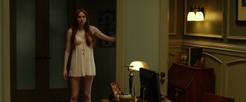 Movie still from “Oculus” (2013), directed by Mike Flanagan – A woman standing in front of a mirror in a room; Medium shot, Over the shoulder angle