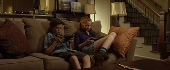 Movie still from “Oculus” (2013), directed by Mike Flanagan – Two children sitting on a couch looking at their phones; Medium shot, High angle