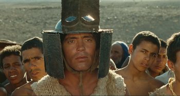 Movie still from “Oedipus Rex” (1967), directed by Pier Paolo Pasolini – A man wearing a metal helmet and some other people in the background; Close Up shot, Low angle
