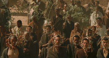 Movie still from “Oedipus Rex” (1967), directed by Pier Paolo Pasolini – A group of people in traditional clothing walking through the streets; Wide shot, High angle