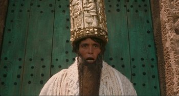 Movie still from “Oedipus Rex” (1967), directed by Pier Paolo Pasolini – A man with a beard wearing a gold hat; Close Up shot, Low angle