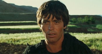 Movie still from “Oedipus Rex” (1967), directed by Pier Paolo Pasolini – A person wearing a sweater near a field; Close Up shot, Over the shoulder angle