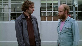 Movie still from “Old Joy” (2006), directed by Kelly Reichardt – Two men standing next to each other in front of a building; Medium shot, Over the shoulder angle