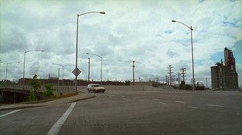 Movie still from “Old Joy” (2006), directed by Kelly Reichardt – An empty street with a car driving down the road; Extreme Wide shot, High angle
