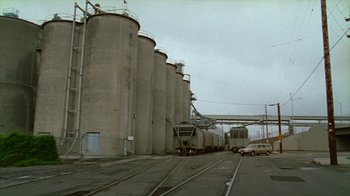 Movie still from “Old Joy” (2006), directed by Kelly Reichardt – A train on the tracks near a large cement building; Extreme Wide shot, Low angle