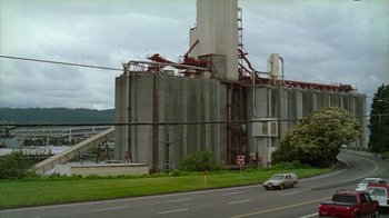 Movie still from “Old Joy” (2006), directed by Kelly Reichardt – A car driving past a large cement building; Extreme Wide shot, Low angle