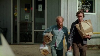 Movie still from “Old Joy” (2006), directed by Kelly Reichardt – Two men walking down the street carrying bags of wood; Wide shot, Low angle