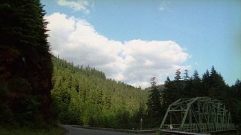 Movie still from “Old Joy” (2006), directed by Kelly Reichardt – A view of a road with trees in the background; Extreme Wide shot, High angle