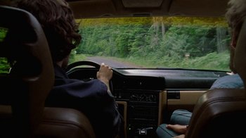 Movie still from “Old Joy” (2006), directed by Kelly Reichardt – A woman driving a car on a road with trees in the background; Medium shot, Over the shoulder angle