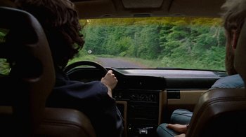 Movie still from “Old Joy” (2006), directed by Kelly Reichardt – A person sitting in the driver's seat of a car driving down a road; Medium shot, Over the shoulder angle