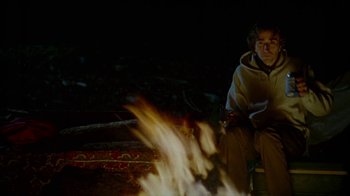 Movie still from “Old Joy” (2006), directed by Kelly Reichardt – A man sitting in front of a fire at night; Medium shot, Over the shoulder angle