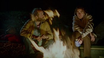Movie still from “Old Joy” (2006), directed by Kelly Reichardt – A couple of men sitting next to each other in front of a fire; Medium shot, Over the shoulder angle