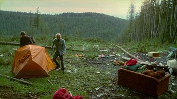 Movie still from “Old Joy” (2006), directed by Kelly Reichardt – A man standing next to an orange tent in the woods; Wide shot, High angle