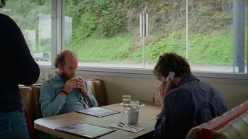Movie still from “Old Joy” (2006), directed by Kelly Reichardt – Two people are sitting at a table talking on their cell phones; Medium shot, Over the shoulder angle