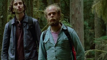 Movie still from “Old Joy” (2006), directed by Kelly Reichardt – A man with a beard is walking through the woods; Medium shot, Low angle