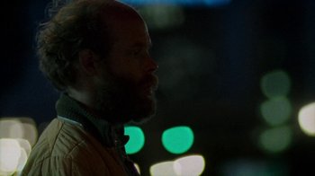 Movie still from “Old Joy” (2006), directed by Kelly Reichardt – A man with a goatee and beard standing in front of blurry lights; Close Up shot, Over the shoulder angle