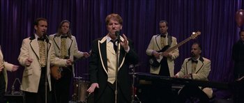 Movie still from “Old School” (2003), directed by Todd Phillips – A man in a tuxedo singing into a microphone; Medium shot, Over the shoulder angle